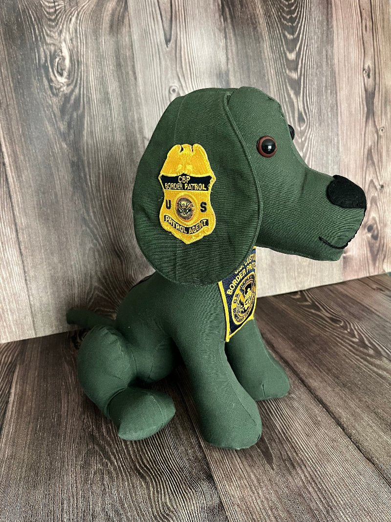 A keepsake memory dog is made from the green uniform of an upcycled border patrol. A yellow and blue badge is sewn on the dog's ear and chest.